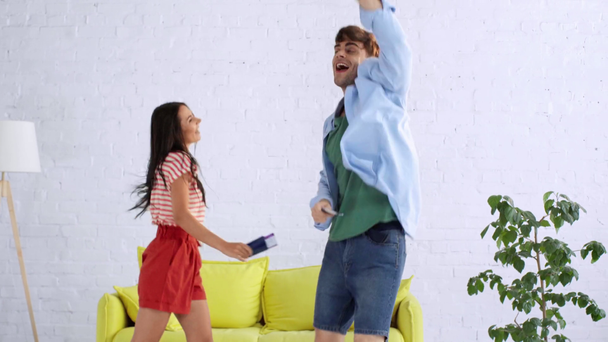 boldog fiatalember és a nő táncol a nappaliban, míg gazdaság útlevél és repülőjegyet - Felvétel, videó