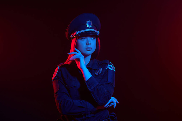 Primer plano de una oficial de policía pelirroja posando para la cámara sobre un fondo negro con retroiluminación roja y azul
. - Foto, imagen