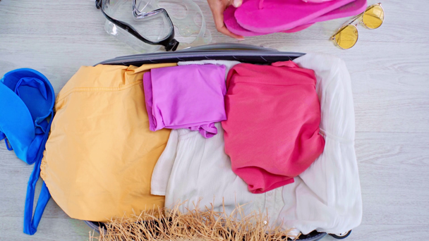 gedeeltelijke weergave van de vrouw verpakking zomer kleren, flip flops en zwemmen masker in koffer op de vloer thuis - Video