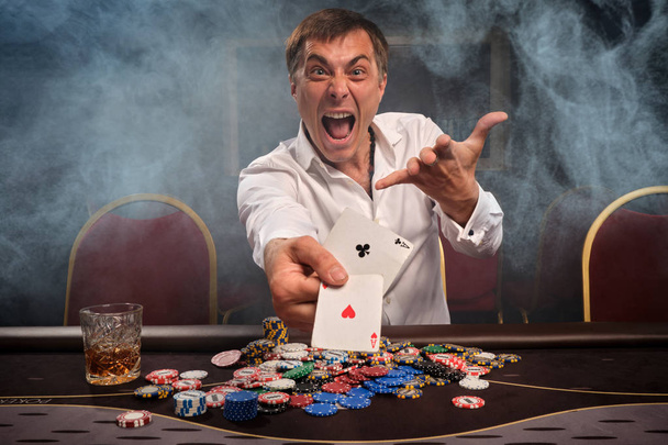 Hezký emocionální muž hraje poker sedí u stolu v kasinu. - Fotografie, Obrázek