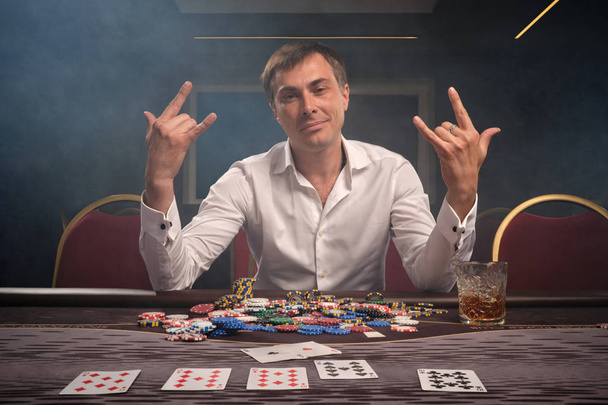 Przystojny emocjonalny mężczyzna gra w pokera siedząc przy stole w kasynie. - Zdjęcie, obraz