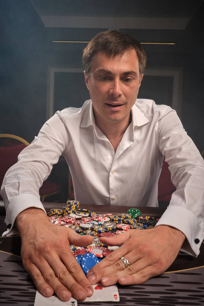 Hezký emocionální muž hraje poker sedí u stolu v kasinu. - Fotografie, Obrázek