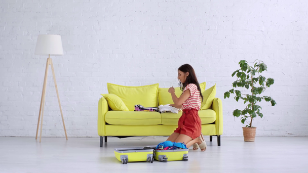 time lapse of pretty young woman unpacking yellow wheeled back and putting clothes on yellow sofa - Footage, Video