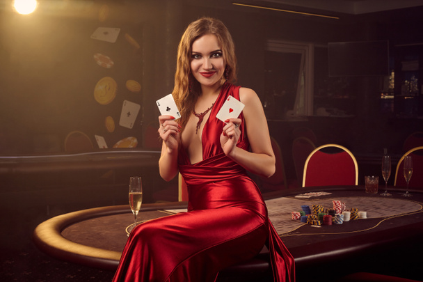 Νεαρή όμορφη γυναίκα ποζάρει ενάντια σε ένα τραπέζι πόκερ στο πολυτελές καζίνο. - Φωτογραφία, εικόνα