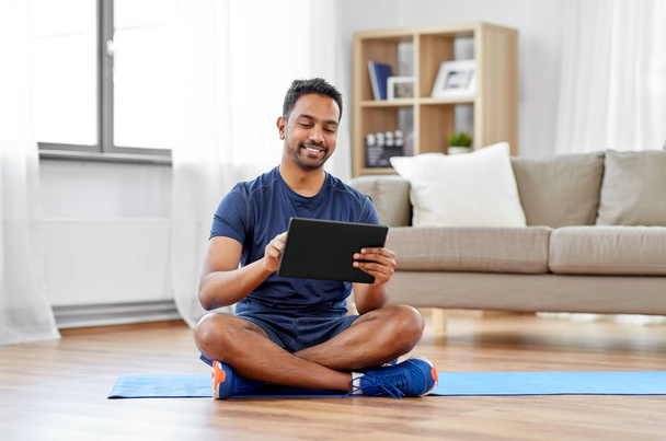 indian man with tablet pc and exercise mat at home - Foto, afbeelding