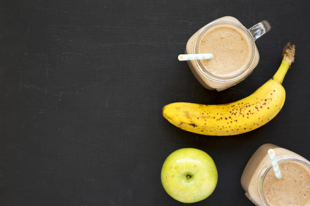 Healthy banana apple smoothie in glass jars over black backgroun - Fotó, kép
