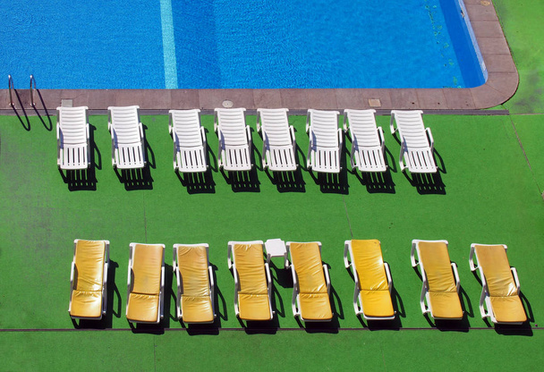 вид сверху на открытый бассейн с солнцезащитными креслами и рябью на воде
 - Фото, изображение
