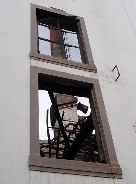 вид через окно заброшенного здания завода с высоким дымоходом, видимым внутри развалин
 - Фото, изображение