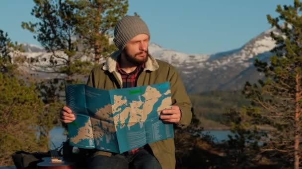 Young brutal man looking a map in a forest at sunset. Norway forest. Wooden table for relaxing. - Metraje, vídeo