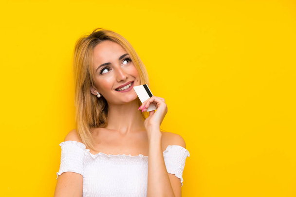 Nuori blondi nainen yli eristetty keltainen seinä tilalla luottokortti
 - Valokuva, kuva
