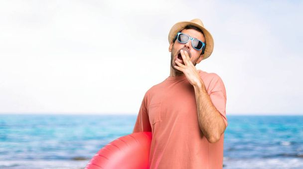 Onun yaz tatili esneme ve el ile geniş açık ağız kapsayan üzerinde şapka ve güneş gözlüğü ile adam. Plajda uykulu ifade - Fotoğraf, Görsel