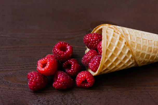 Свежая малина в вафельном конусе на коричневом деревянном фоне. концепция меню из сладких фруктов. Малиновое мороженое. органические продукты
 - Фото, изображение