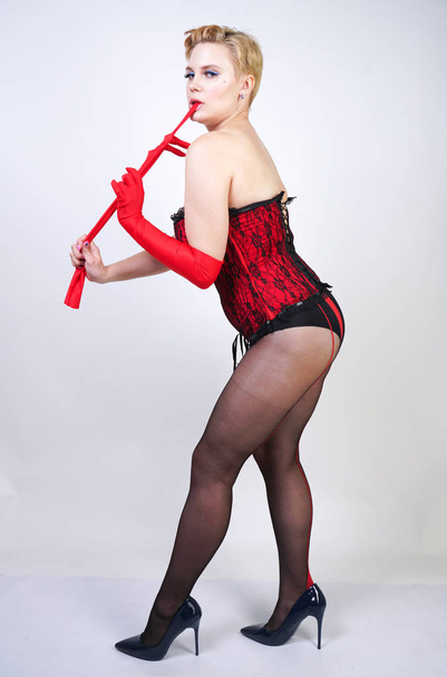 сексуальна жінка плюс розмір жінка з коротким волоссям в червоному мереживному боді і класичні чорні колготки з швом позує на білому тлі в студії
 - Фото, зображення