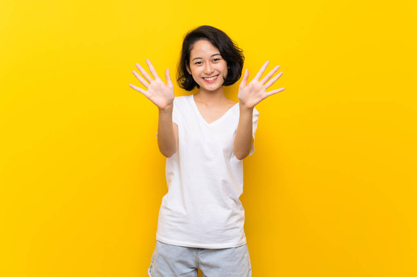 asiatische junge Frau über isolierte gelbe Wand, die mit den Fingern zehn zählt - Foto, Bild
