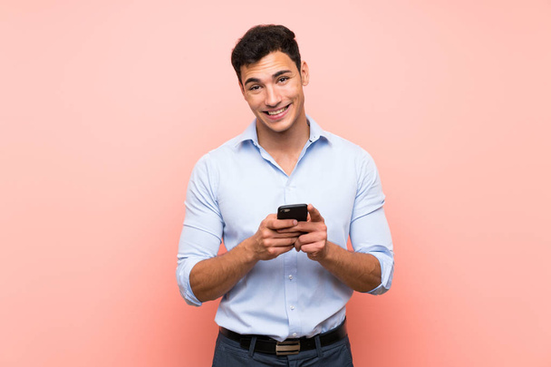 Jóképű férfi rózsaszín háttér küld egy üzenetet a mobil - Fotó, kép