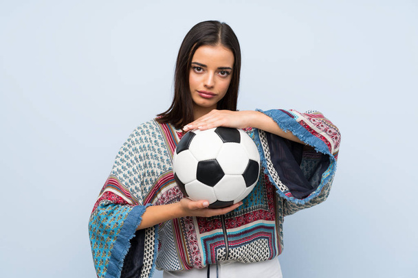 Молода жінка над ізольованою синьою стіною тримає футбольний м'яч
 - Фото, зображення