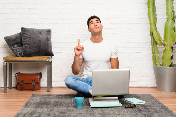 Handsome man sitting on the floor with his laptop pointing with the index finger a great idea - Фото, изображение