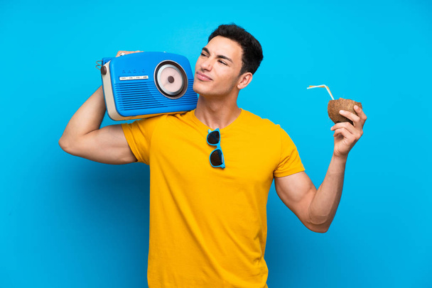 Handsome man over blue background holding a radio - 写真・画像