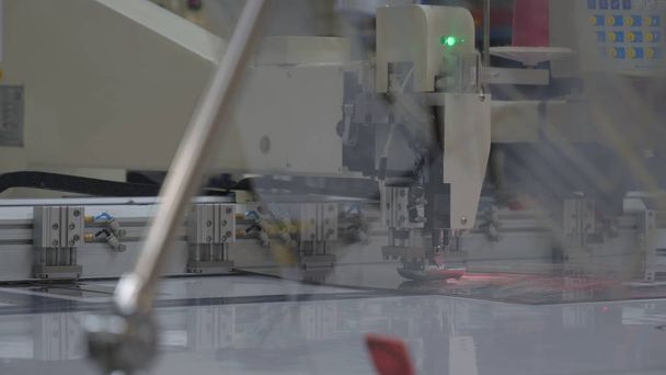 In der industriellen Bekleidungsfabrik schneidet ein spezielles Laserschneidegewebe bestimmte Textilteile aus. Konzept: Lasermaschine, Kreuze, Arbeit in einer Fabrik, automatisches Schneiden. - Foto, Bild