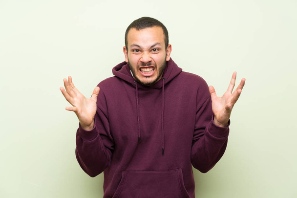 colombiano homem com camisola sobre parede verde infeliz e frustrado com algo
 - Foto, Imagem
