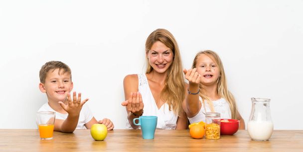 Mère avec ses deux enfants prenant le petit déjeuner faisant geste à venir
 - Photo, image