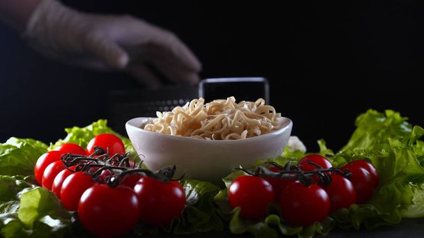 Im Hintergrund Salatblätter und ein Holztisch, ein Fertiggericht aus Gemüsenudeln und ein Meer von Produkten werden festgehalten und dann mit chinesischen Stöcken probiert (gegessen). Konzept: Garnelen, Gemüse - Foto, Bild