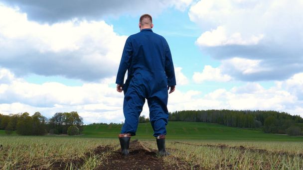 Farmer in a working uniform, walks across a field in rubber boots, A young guy (man), a farmer in a working uniform, stands in a field and inhales deeply, feeling freedom on a sunny day. Concept of: Freedom, Breathing, Lifestyle, Farmer, Heaven, Slow - Foto, Bild