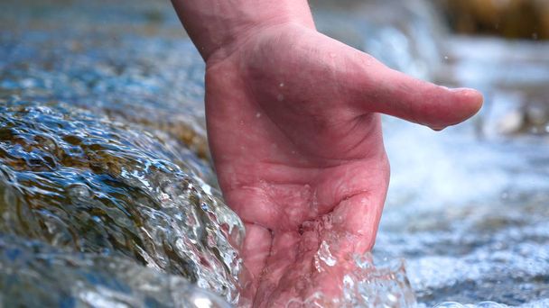 A man holds his hand (washes his hands) in the fountain (water), clearing them of dirt, and holding the water of the waterfall in the length of his hand. Concert of: Feel the water, Slow motion. - Foto, Imagem