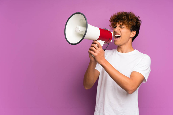 Молодий афроамериканець над ізольованою фіолетовою стіною кричить через мегафон. - Фото, зображення
