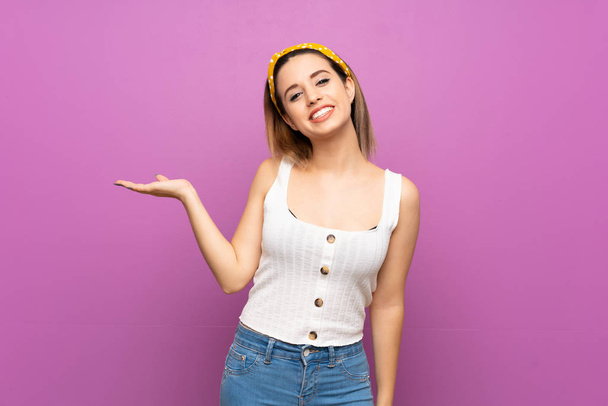 Krásná mladá žena nad izolovanou purpurovou stěnou držící v dlani copyspace imaginární pro vložení reklamy - Fotografie, Obrázek