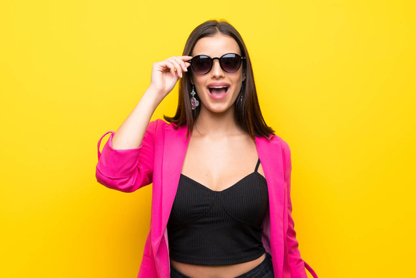 Young woman over isolated yellow background with glasses and surprised - Φωτογραφία, εικόνα