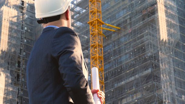 Rakentaja tai insinööri, seisoo selkä katsomassa rakennuksia, yllään valkoinen kypärä ja yllään puku, puhuu puhelimessa, pilvenpiirtäjä
 - Valokuva, kuva