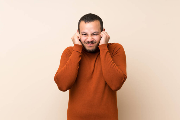 Kolumbijský muž s rotleneck svetrem frustrovaný a zakrývající uši - Fotografie, Obrázek