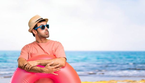 Man with hat and sunglasses on his summer vacation having doubts and with confuse face expression while bites lip. Questioning an idea at the beach - Photo, Image