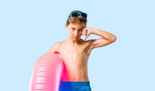 Дитина на літніх канікулах показує знак великого пальця вниз з негативним виразом на ізольованому синьому фоні
 - Фото, зображення