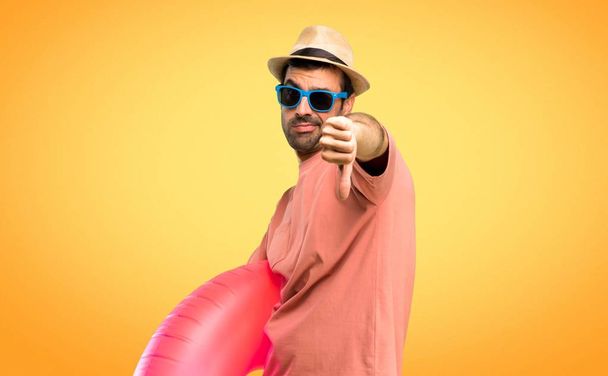 Mann mit Hut und Sonnenbrille im Sommerurlaub zeigt Daumen-runter-Zeichen mit negativem Ausdruck auf orangefarbenem Hintergrund - Foto, Bild
