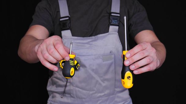 der Meister, Baumeister oder Reparateur hält einen Bremssattel in der Hand, in einem speziellen Anzug, einem gelben Maßband mit Messgrößen, schwarzem Hintergrund. - Foto, Bild