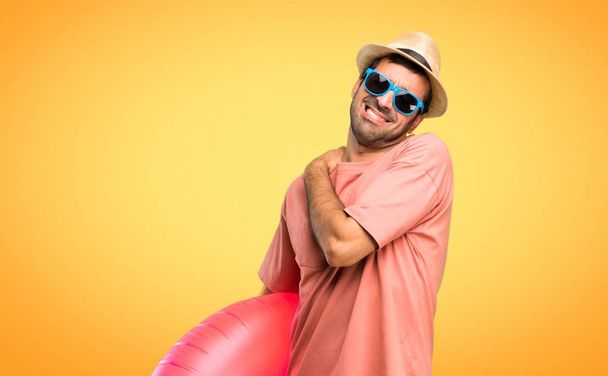 Άνθρωπος με καπέλο και γυαλιά ηλίου στις καλοκαιρινές του διακοπές που υποφέρουν από πόνο στον ώμο για να έχουν κάνει μια προσπάθεια σε πορτοκαλί φόντο - Φωτογραφία, εικόνα