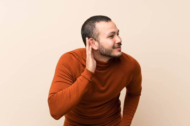 Colombian man with turtleneck sweater listening to something by putting hand on the ear - Foto, Imagem
