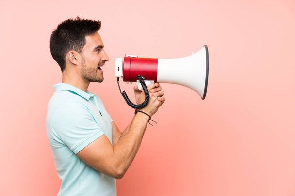 Handsome young man over isolated background shouting through a megaphone - Photo, Image