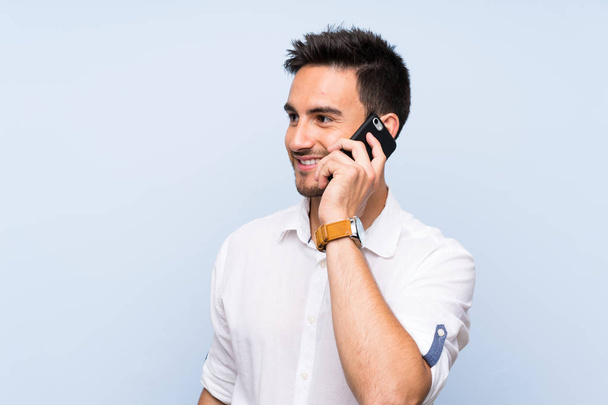 Handsome young man over isolated blue background keeping a conversation with the mobile phone - Foto, Imagem