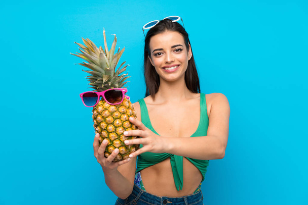 Young woman in swimsuit in summer holidays holding a pineapple with sunglasses - Foto, afbeelding