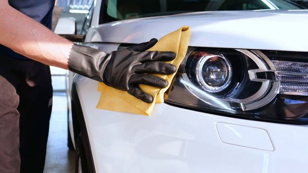 Professional car washer wipes and dries window after car washing service. Concept from: Reading glasses, Professional work, Black gloves, Blue rag - Foto, Bild