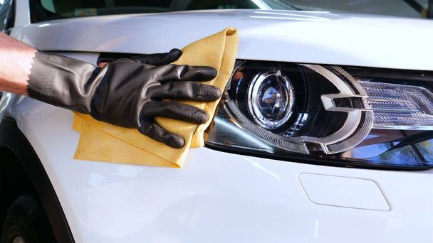 Professional car washer wipes and dries window after car washing service. Concept from: Reading glasses, Professional work, Black gloves, Blue rag - Photo, image