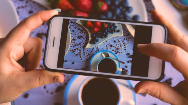 A girl or a woman takes a photo of food, breakfast, coffee, donuts, strawberries, coffee, A cup of coffee and coffee beans, blueberries and strawberries. - Foto, Imagem
