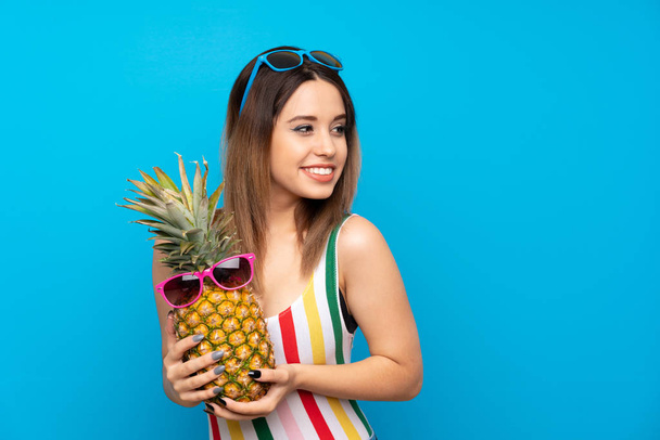 Jonge vrouw in de zomervakantie over blauwe achtergrond met een ananas met een zonnebril - Foto, afbeelding
