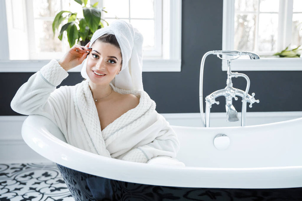 Мила молода жінка з рушником на голові сидить у ванній
 - Фото, зображення