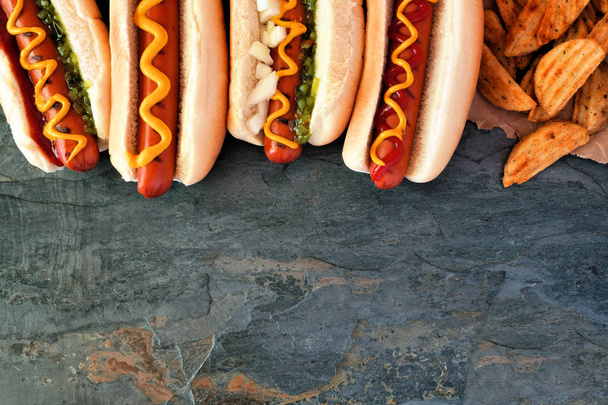 Hot dog con guarnizioni e spicchi di patate. Bordo superiore, vista aerea su uno sfondo di pietra scura con spazio di copia
. - Foto, immagini
