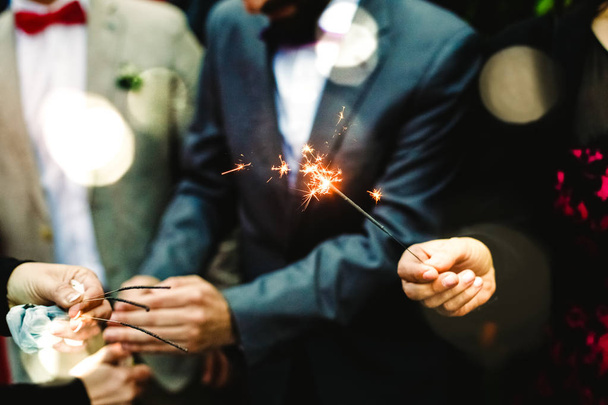 Hombres elegantes sosteniendo una bengala encendida durante una fiesta
 - Foto, Imagen