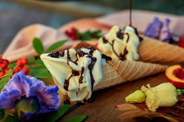 Морозиво в конус наливають топінгом, прикрашеним квітами на дерев'яний стіл. Концепція дисплея морозива
. - Фото, зображення